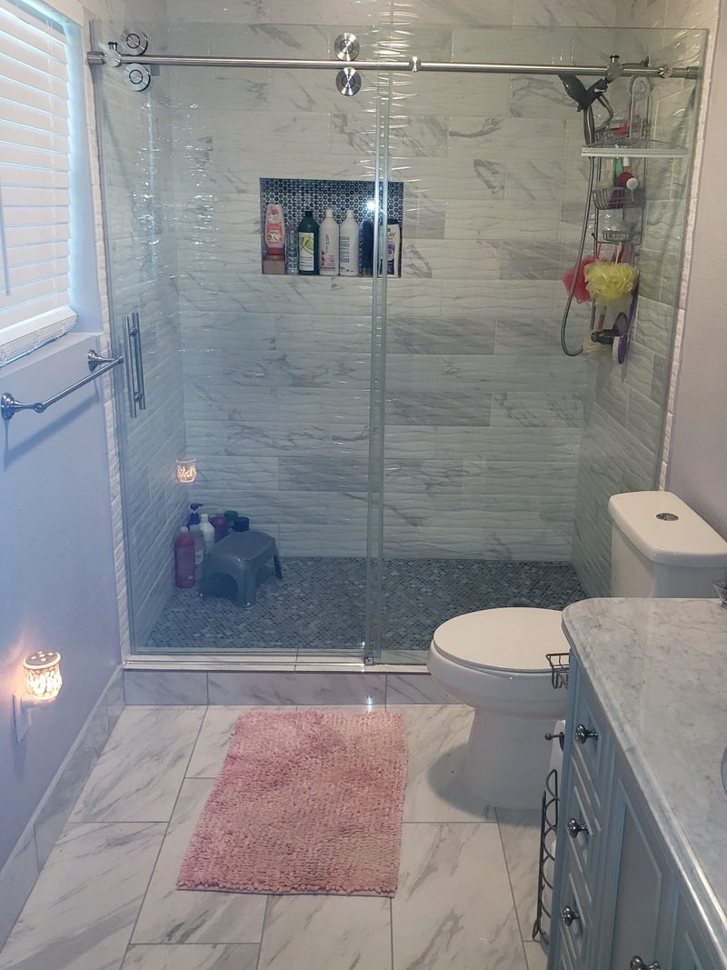 Finished bathroom renovation with marble tile and glass shower.
