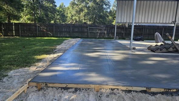 A finished backyard concrete slab formed and poured by Level Headed Construction beside a metal building