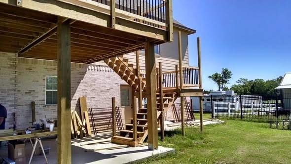An elevated wood deck with a switchback staircase built off the back of a brick home by Level Headed Construction in the Lake Houston area