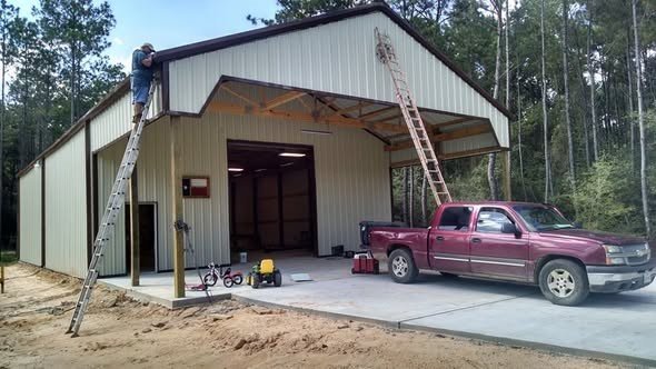 A metal building under construction with a maroon pickup parked under the open bay, showing carport and metal awning work in the Lake Houston area