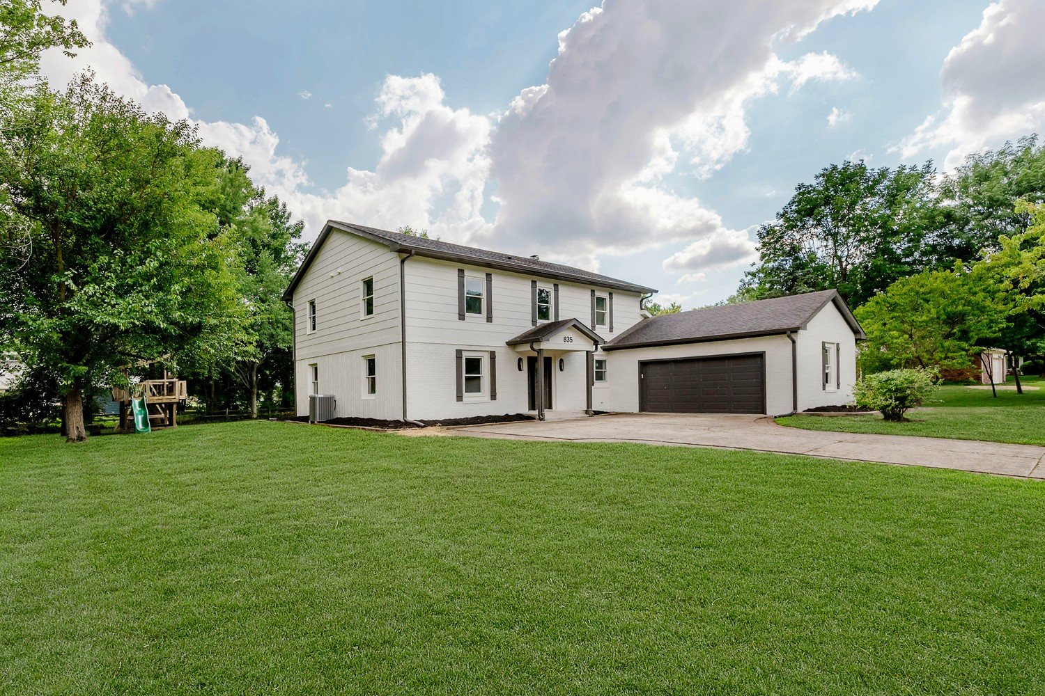 Two-story home with fresh white siding, a dark composition-shingle roof, attached two-car garage, and a manicured lawn under a blue sky.
