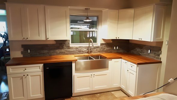 A finished kitchen remodel by Level Headed Construction with cream cabinets, a butcher-block island top, stainless farmhouse sink, and a stacked-stone backsplash