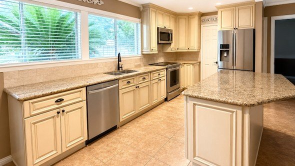 A finished kitchen remodel by Level Headed Construction — cream raised-panel cabinets, a center island, granite-look counters, and tile floor in a Huffman-area home