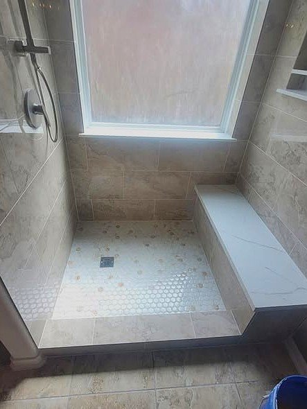 A walk-in shower by Level Headed Construction with a built-in bench and mosaic floor, tiled wall-to-wall with a recessed niche