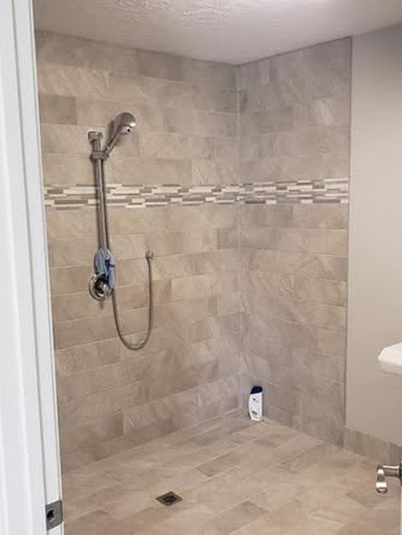 A low-threshold walk-in shower by Level Headed Construction with a handheld fixture and continuous tile floor for easier, safer access