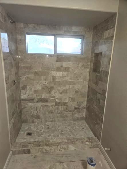 A walk-in tile shower by Level Headed Construction in travertine-look stone with an open entry, recessed niche, and a window in a Huffman-area bathroom