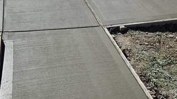 A finished concrete walkway with broom-textured joints poured by Level Headed Construction alongside a lawn