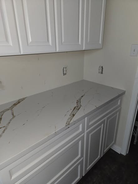 A remodeled kitchen by Level Headed Construction with new white cabinetry and a veined stone-look waterfall-edge countertop