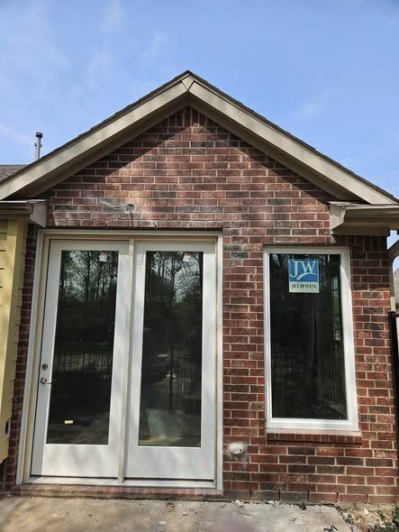 A newly installed white window and patio door in a brick wall, the window still wearing its factory sticker, on a home in the Huffman / Lake Houston area