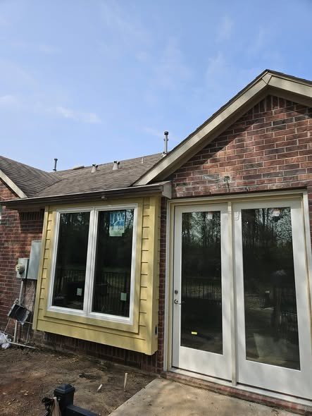 A new white window and glass patio door at the back corner of a brick home in the Lake Houston area, freshly installed and trimmed