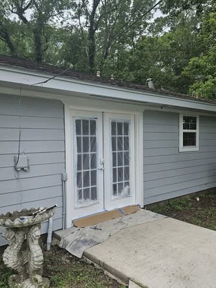 A new white French-style patio door and window installed in gray lap siding on a home in the Huffman / Lake Houston area