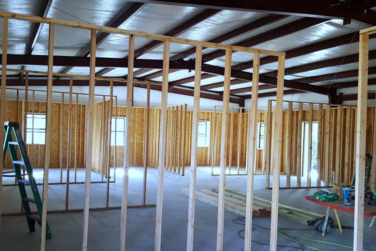 Interior of a Level Headed Construction jobsite: steel-beam ceiling with dimensional-lumber wall framing dividing a new building into rooms, daylight pouring through window openings